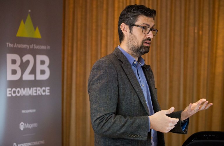 A man standing and gesticulating as he speaks in front of a sign that says B2B eCommerce
