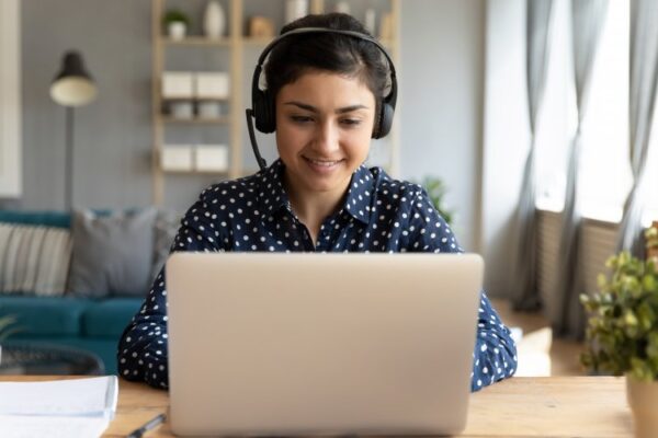 Woman types on laptop wearing a headset.