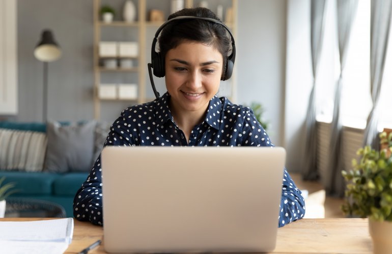 Woman types on laptop wearing a headset.