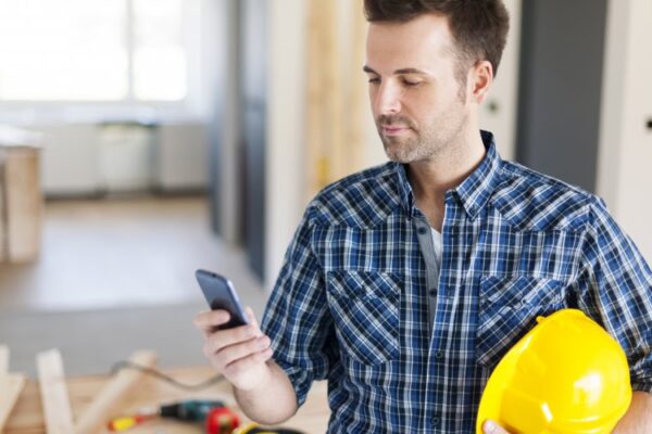 Man holds a hardhat and uses mobile phone