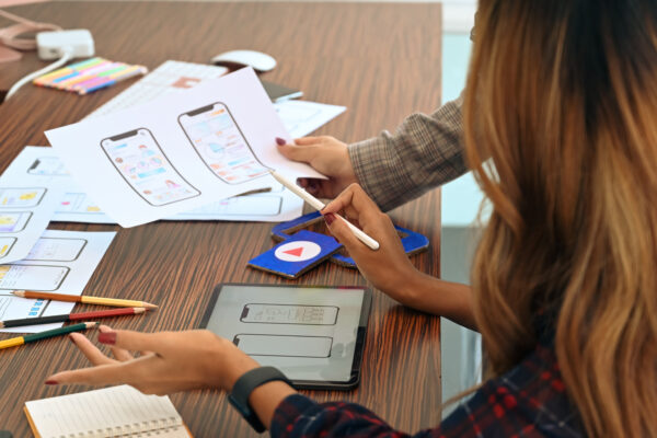 Two designers work on printed mobile designs on a table