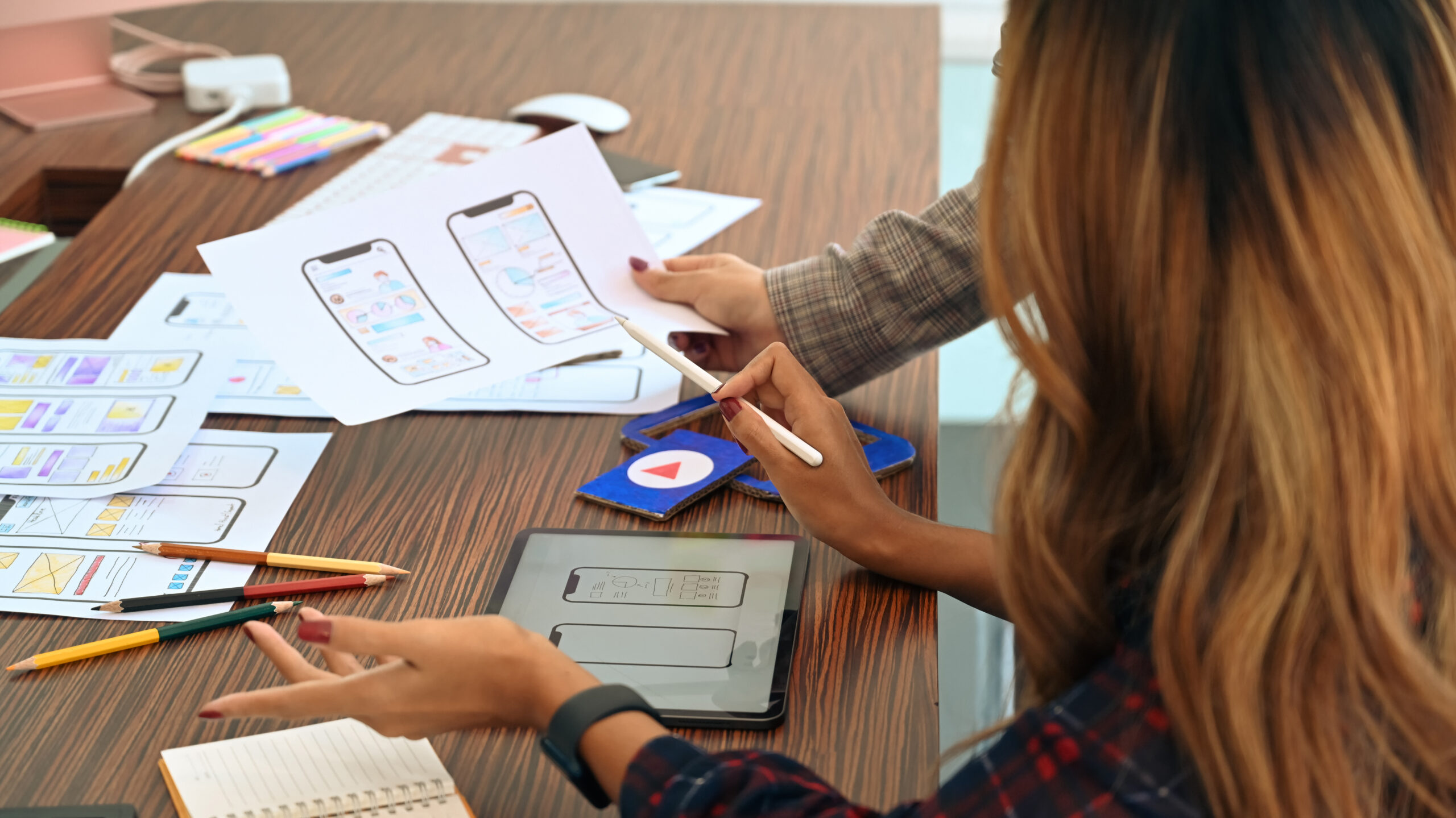 Two designers work on printed mobile designs on a table