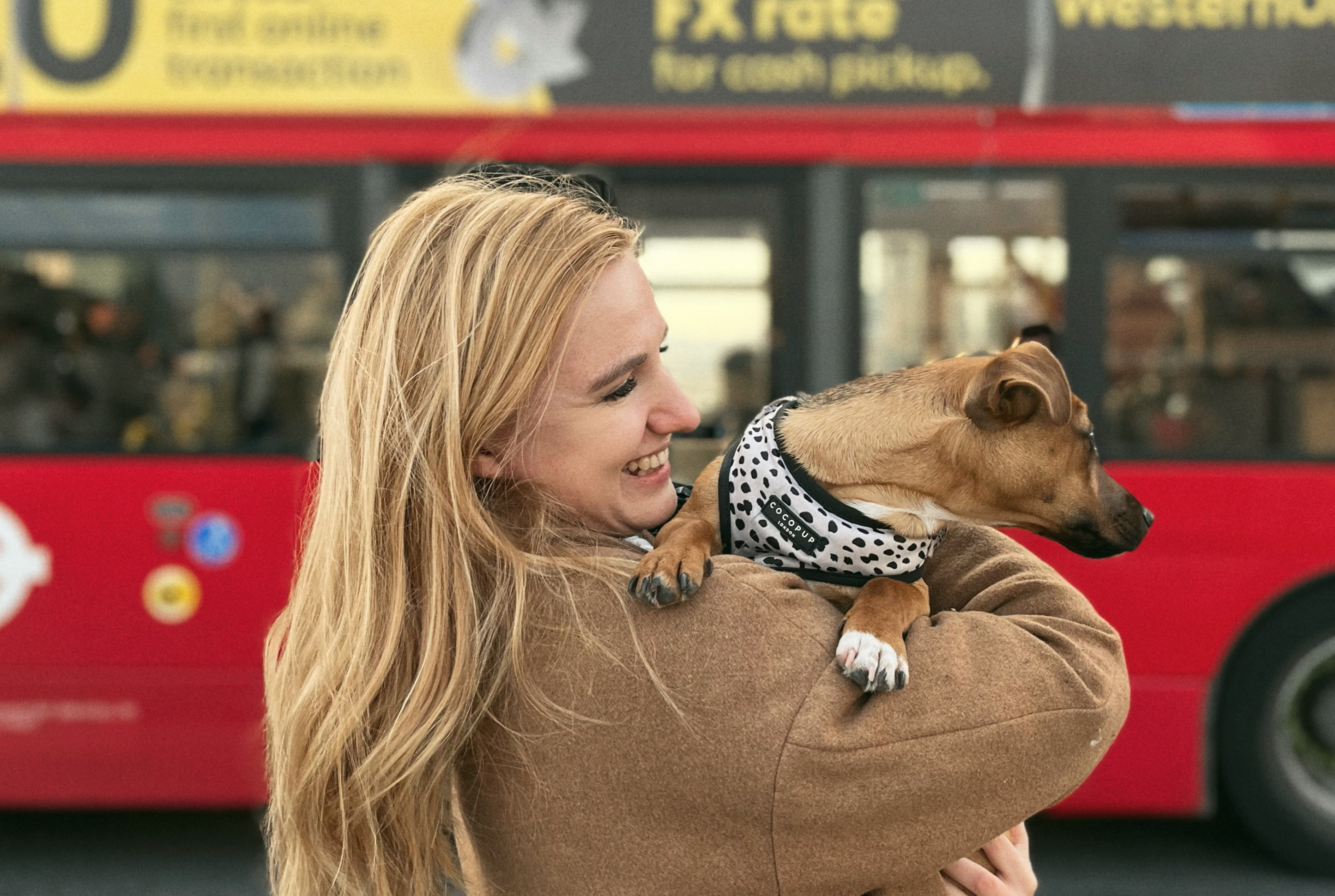 A blonde woman holds a dog in front of a red bus