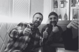 Two men seated giving thumbs up